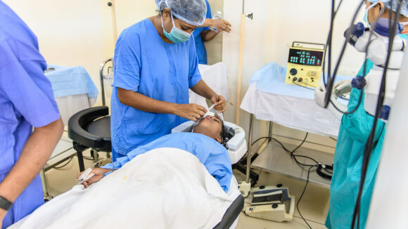 Archana is having a cataract operation. A doctor stands over Archana while they are working on Archana's eye.