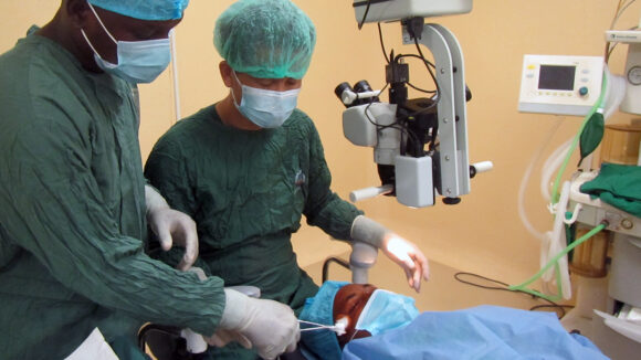 Two surgeons in green scrubs carrying out an eye operation.