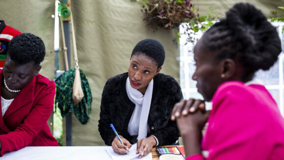 Three women at a desk, one is writing on paper.