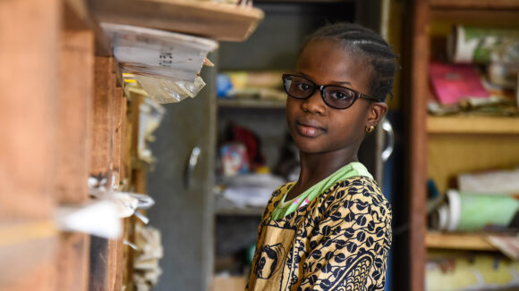 A young girl smiles as she stands in a classroom.