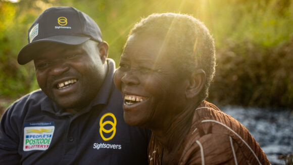 Mai Mai smiles with a patient as the sun shines behind them.