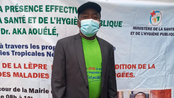 Sightsavers Konan Nguessan stands in front of an event sign written in French.