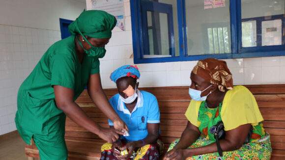 A woman wearing medical scrubs speaks to two women, one with a bandage over her left eye.