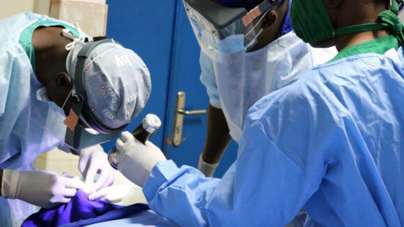 A group of doctors in blue surgical scrubs performing eye surgery.