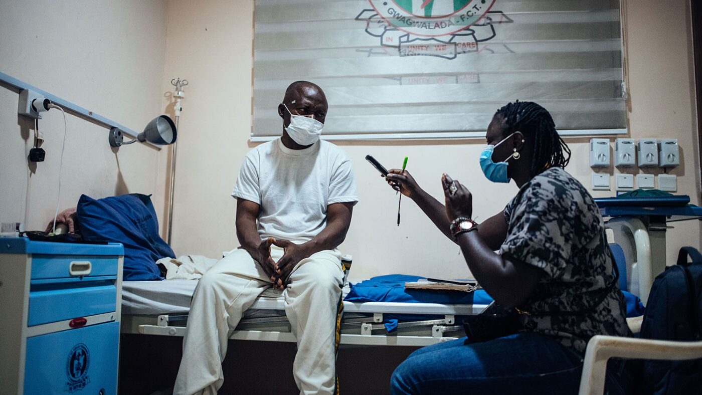 A man sitting on a hospital bed is interviewed by a Sightsavers staff member.