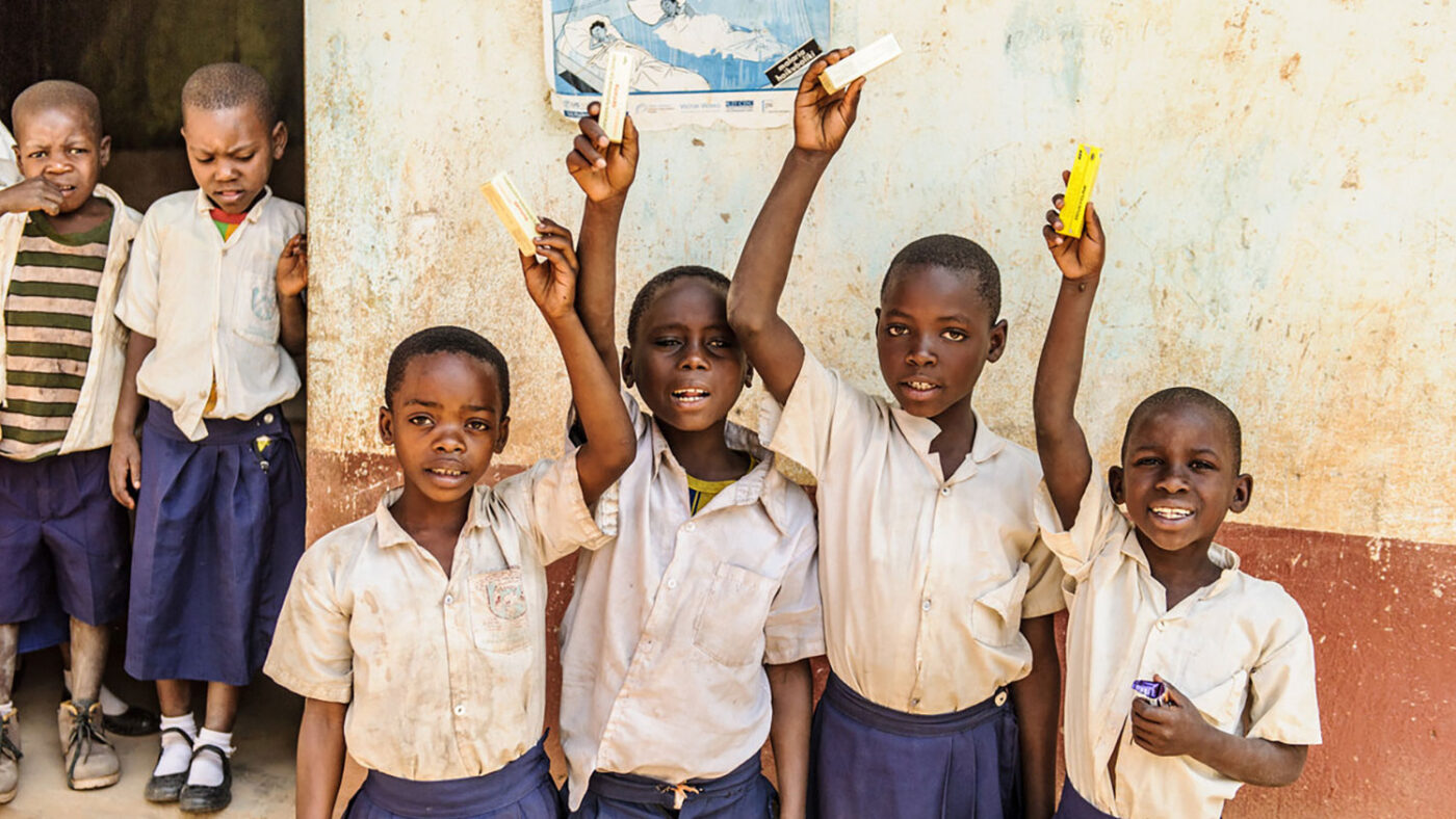 A group of young children in uniform smile and hold up their treatment following an eye health screening.