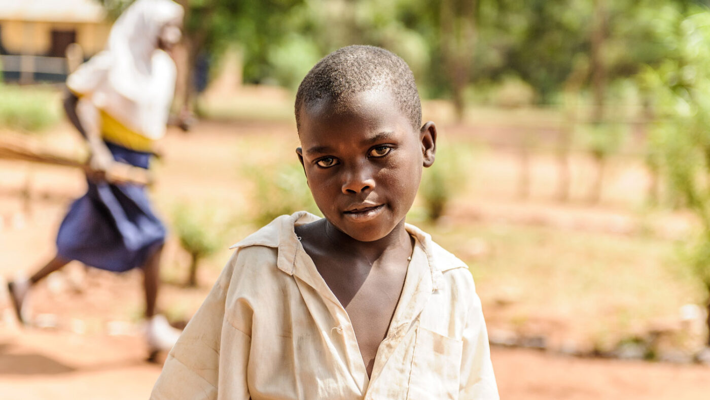 A young girl stands outside in school uniform.