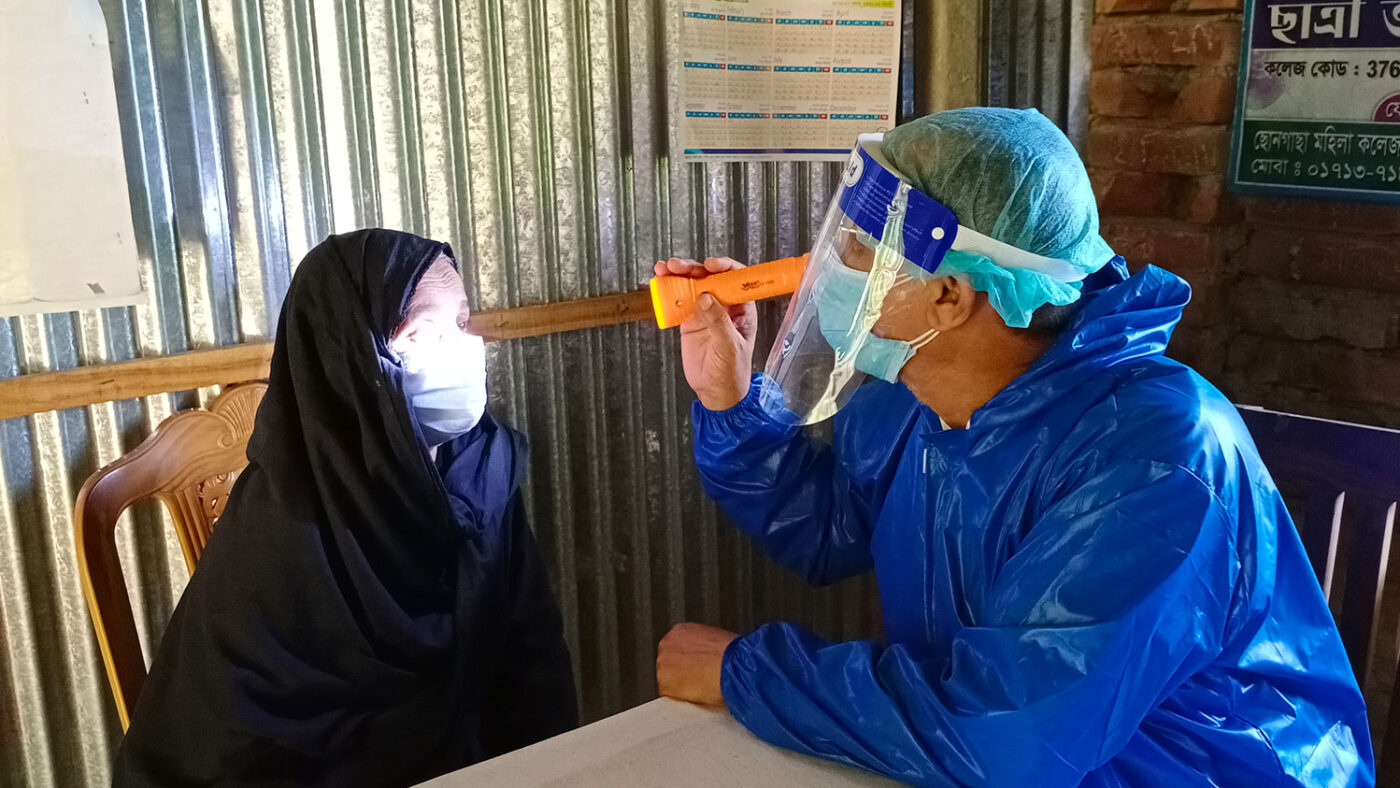 A woman's eyes are examined by a health worker wearing PPE.