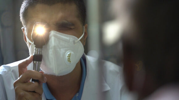 A doctor holds a torch and examines a man's eyes.