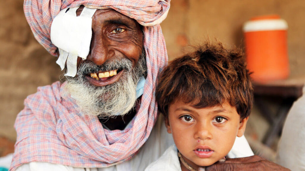 A man with a bandage over his right eye smiles for a photo with his young grandson.
