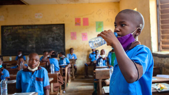 In Cameroon, a schoolboy in a classroom has a drink of water after taking deworming medication.