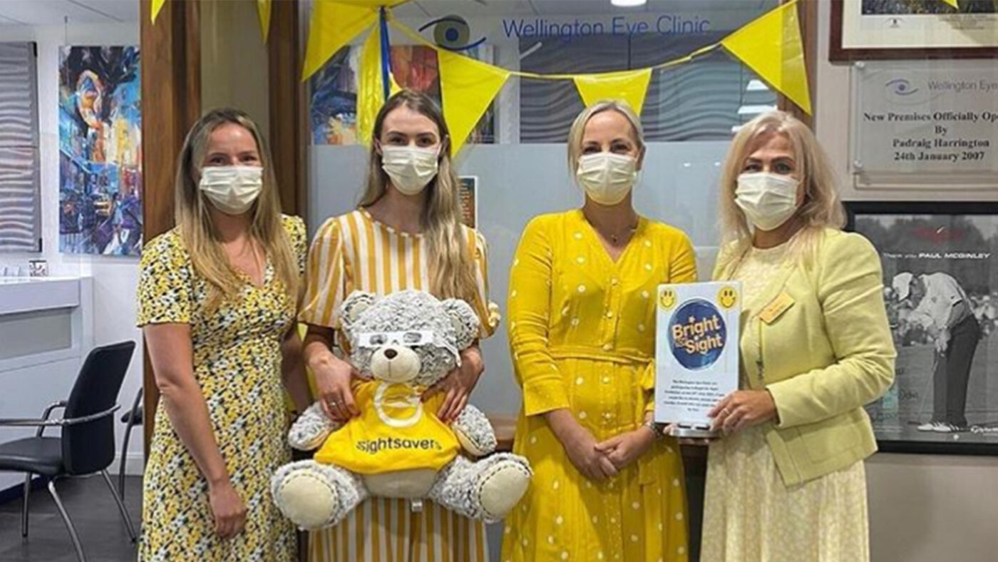 Four people wearing bright yellow outfits and holding a sign saying 'Bright for Sight'.