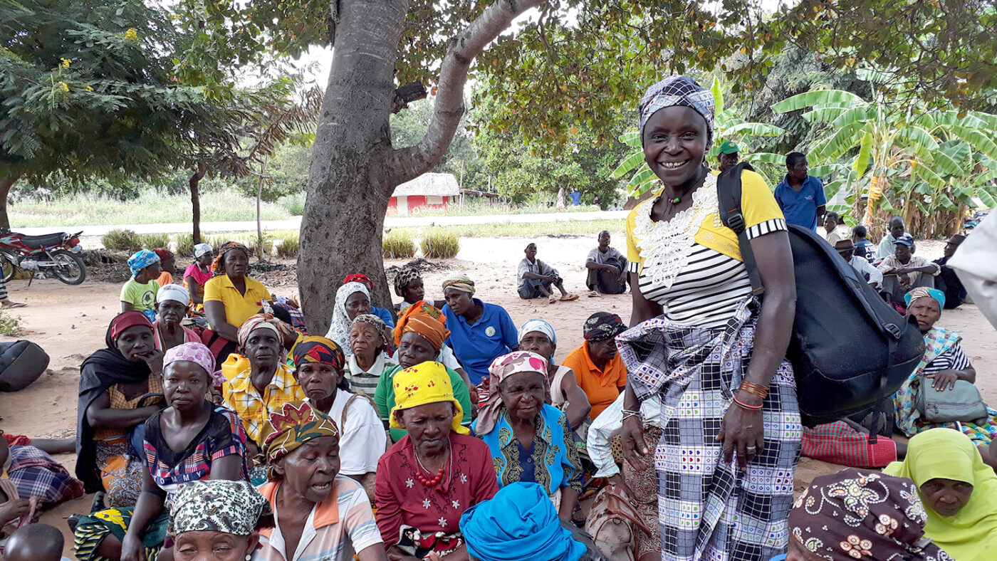 Deolinda stands smiling surrounded by a group of older women who are sitting down.
