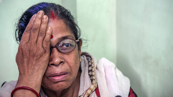 A woman wearing glasses holds one hand over her right eye during an eye test.