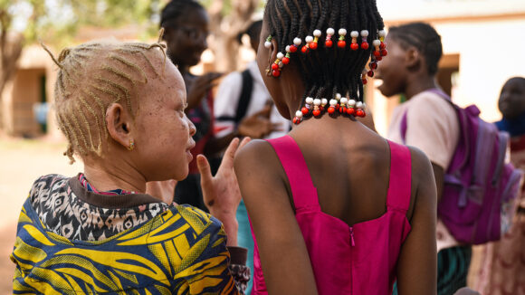 A schoolgirl wearing colourful clothing talks to a friend in the playground at their school in Mali.