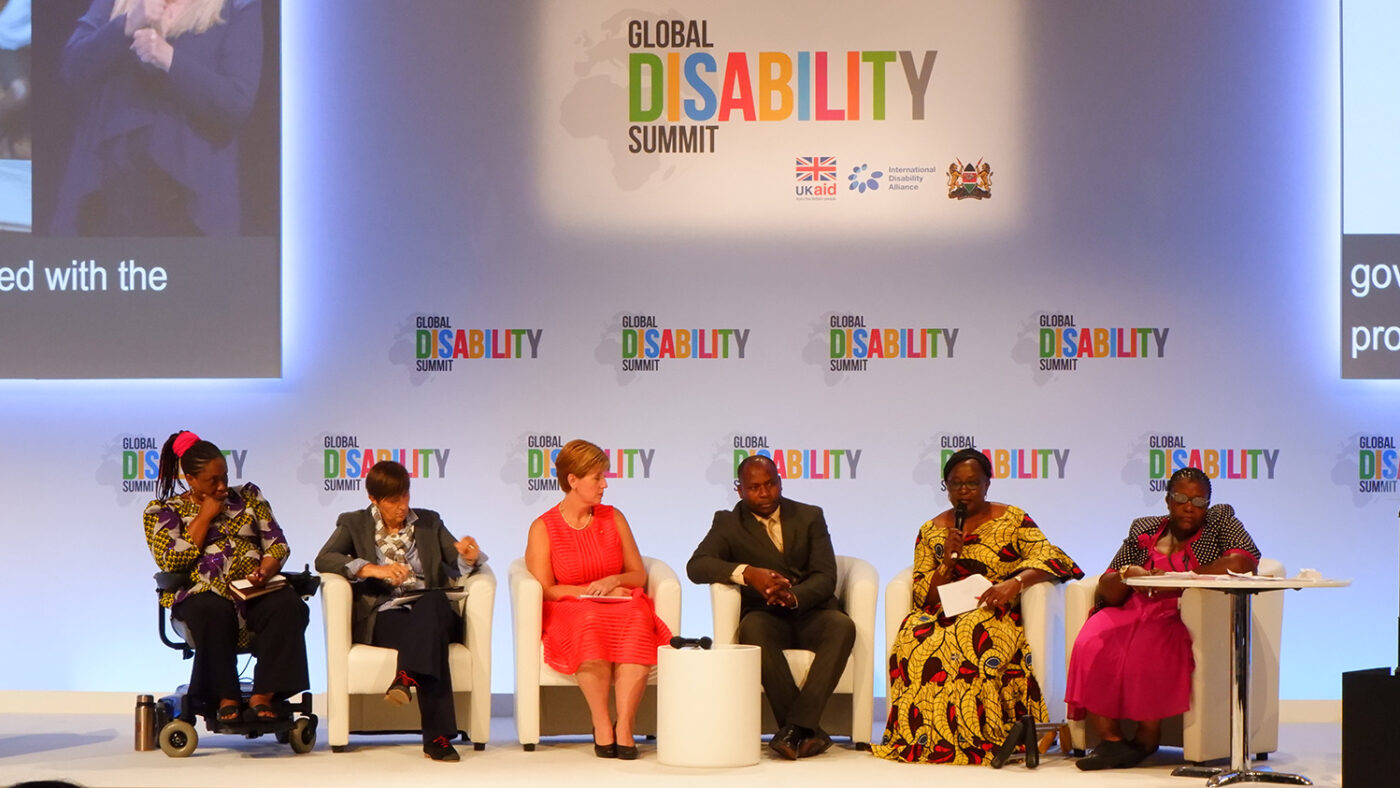 A panel of six speakers sit on stage at the Global Disability Summit in 2018.