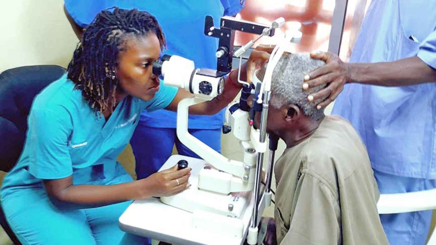 Dr Jalikatu uses ophthalmology equipment to examine a man's eyes.
