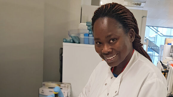 Pelagies smiles while standing in a laboratory.