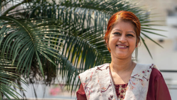 Asma stands smiling in front of a large palm tree.