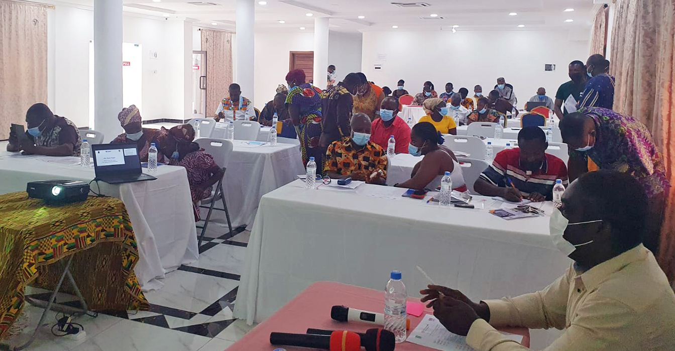 A large group of people sit at tables in a room where they are receiving training to become inclusion ambassadors.