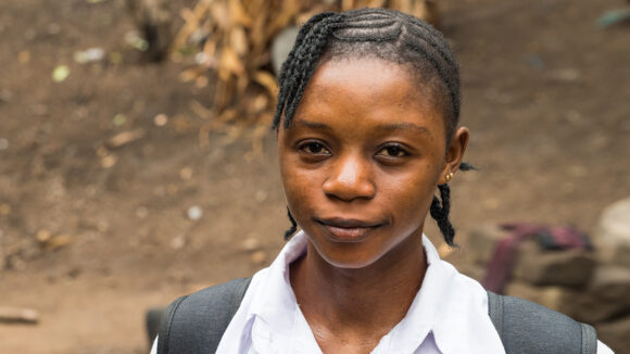 Saio stands outside wearing her school uniform and backpack.