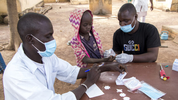Two health workers wearing surgical masks takes a blood sample from a young boy's finger..