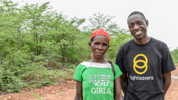 Ophthalmic nurse Jeremiah Gwafa smiles as he stands next to a local community member.