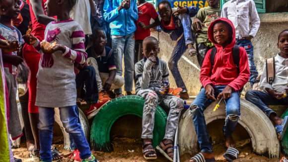 Ousmane, a young student with a physical disability is surrounded by friends in the playground during break time at school.