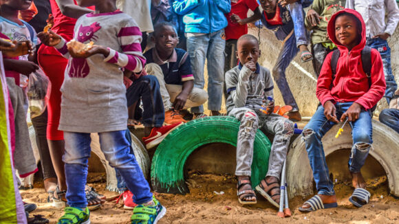 A boy with crutches sits with his friends in the playground during lunch break at school in Senegal.