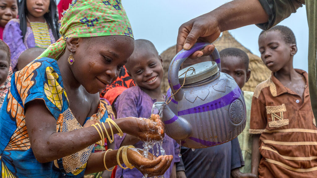 Ophthalmic nurse Suraju helps a young girl wash her hands using water from a teapot.