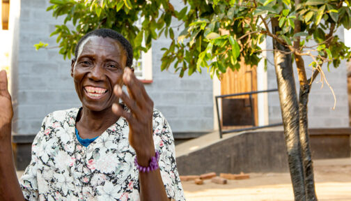 Vainesi smiles and claps outside her home in Malawi.