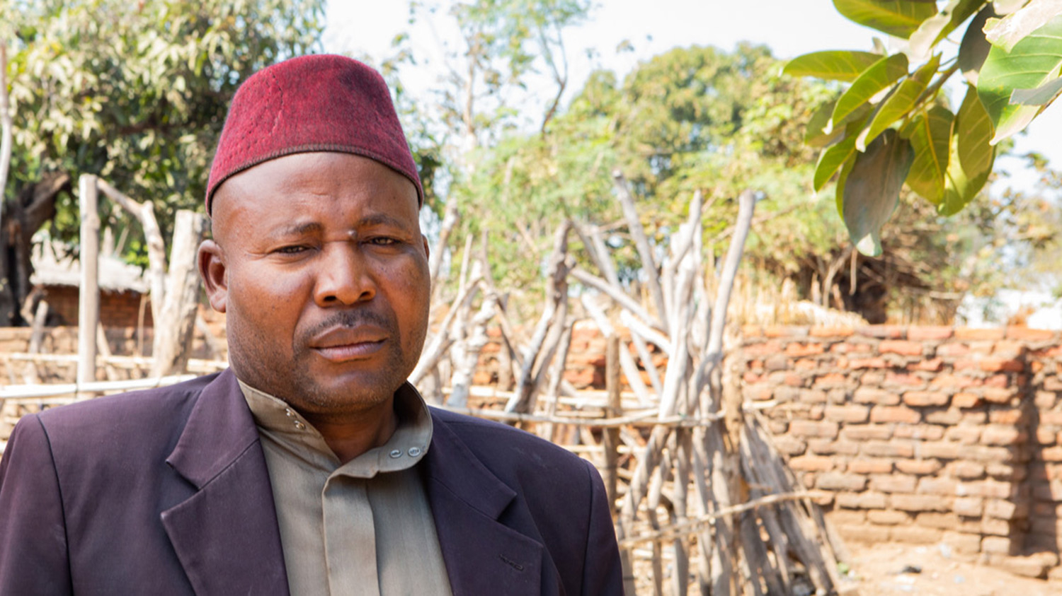 Chief Maganga wears a red hat and smart clothes in his village.