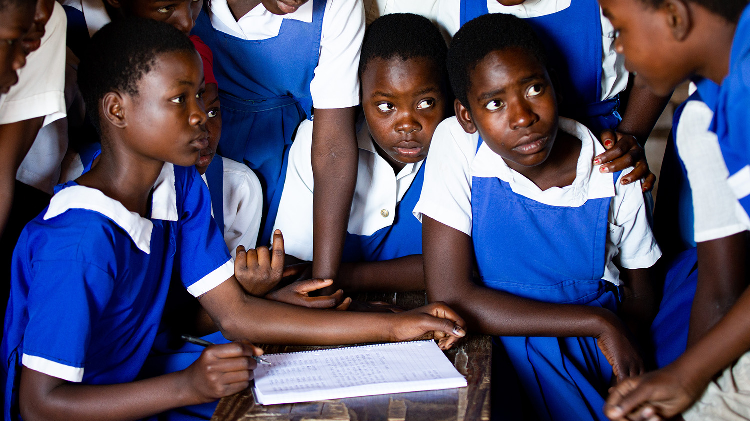 Students from the club gather round a desk and talk. They're wearing their bright blue uniforms.