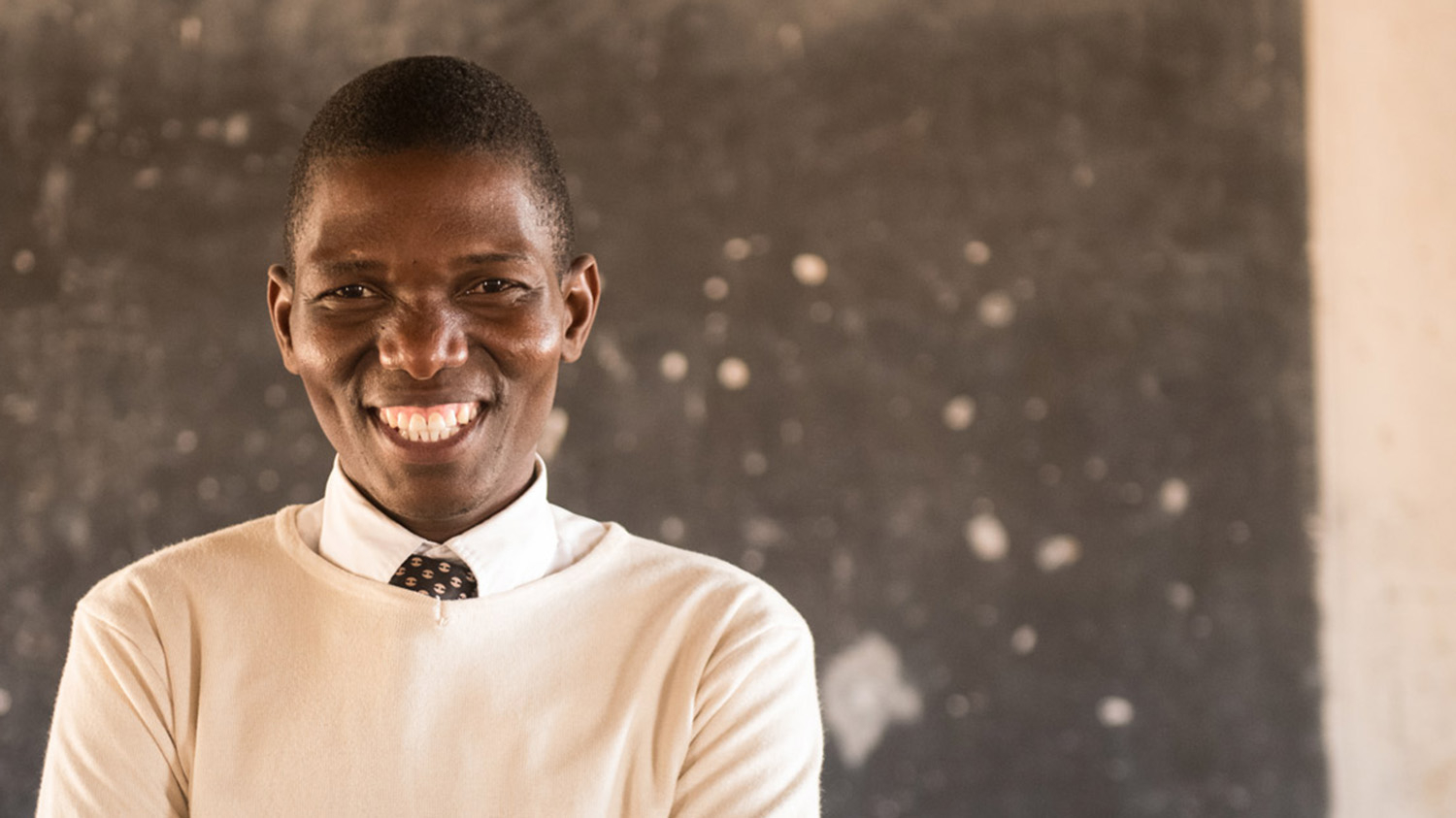 Francis stands in front of his blackboard in the classroom, smiling broadly.
