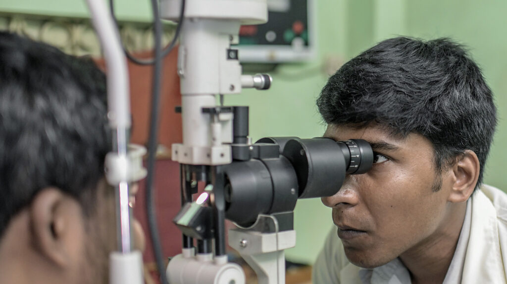 A health care worker checks someone's eyes using examination equipment.