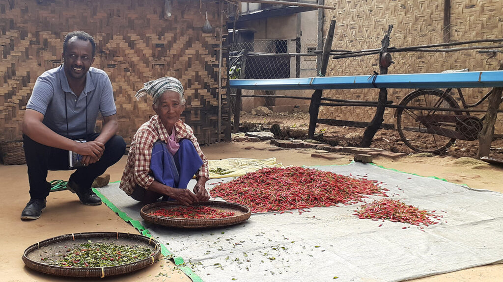 Epidemiologist Michael Dejene, who is collecting data on trachoma, crouches next to a woman who is sorting produce.