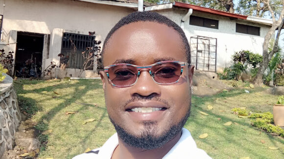Alinafe smiles while standing outside a house.