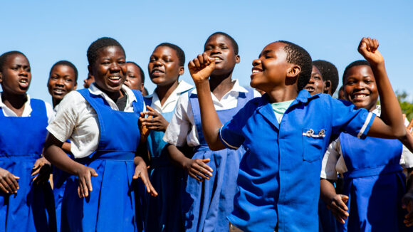 School students from Malawi smile and dance outside in the sunshine.