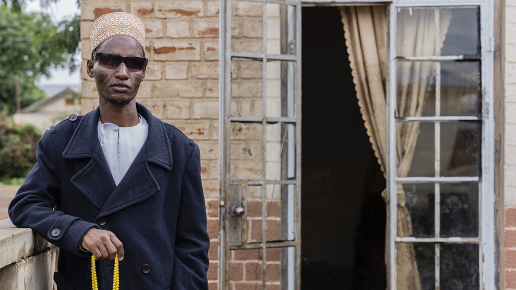 Hamis, who is blind, poses outside his home while holding prayer beads.