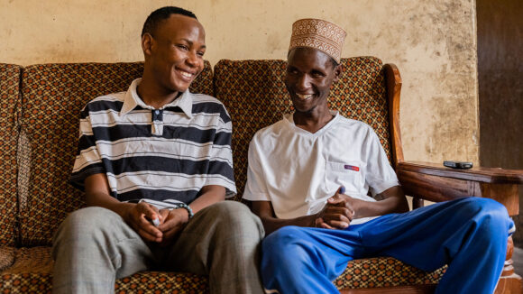 Hamish. who is blind, sits on sofa alongside his younger brother Abubakari at their home in Tanzania.