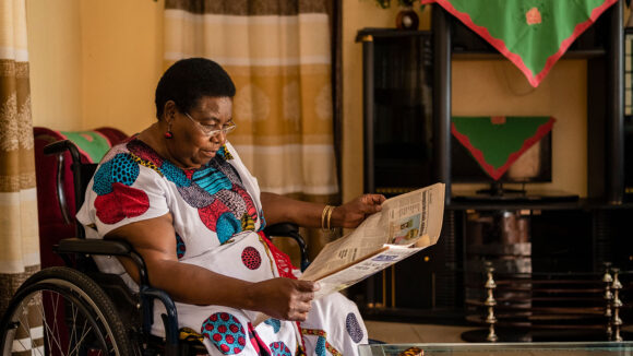 OPD leader Sarah reads a newspaper while sitting in her wheelchair at home.