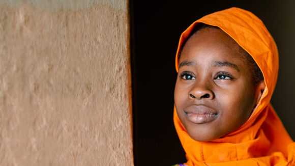 Khadijah smiles while wearing a vibrant orange headscarf.