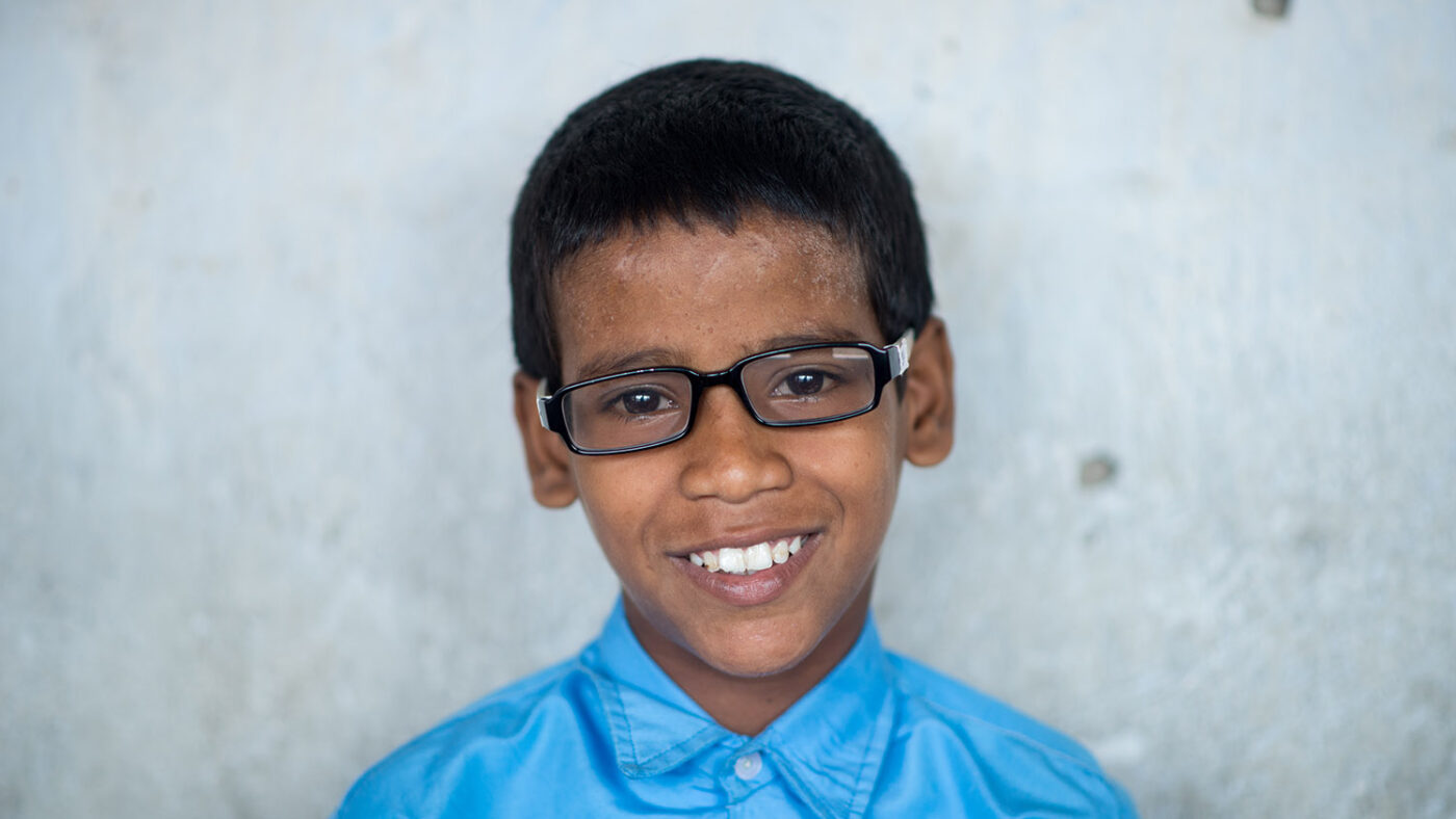 Shahid smiles for a portrait wearing his glasses.