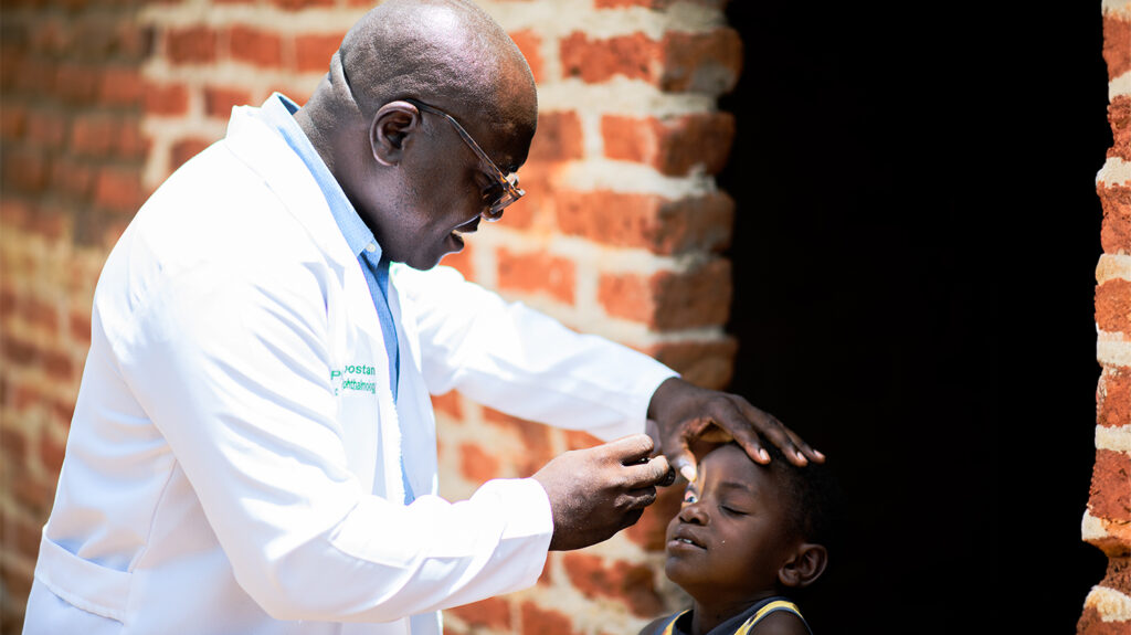 A doctor in a white coat shines a light into a young child's eyes to check for eye conditions.