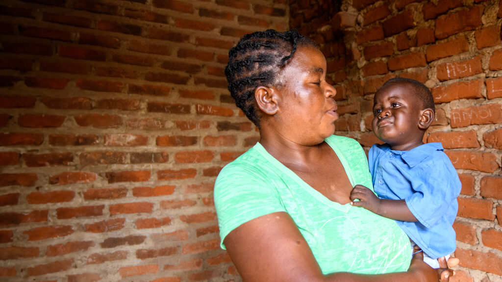 A mother holds and looks at her young son as they stand in front of a brick wall.