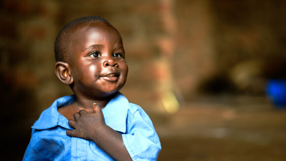 A young boy wearing a smart blue shirt smiles sweetly.