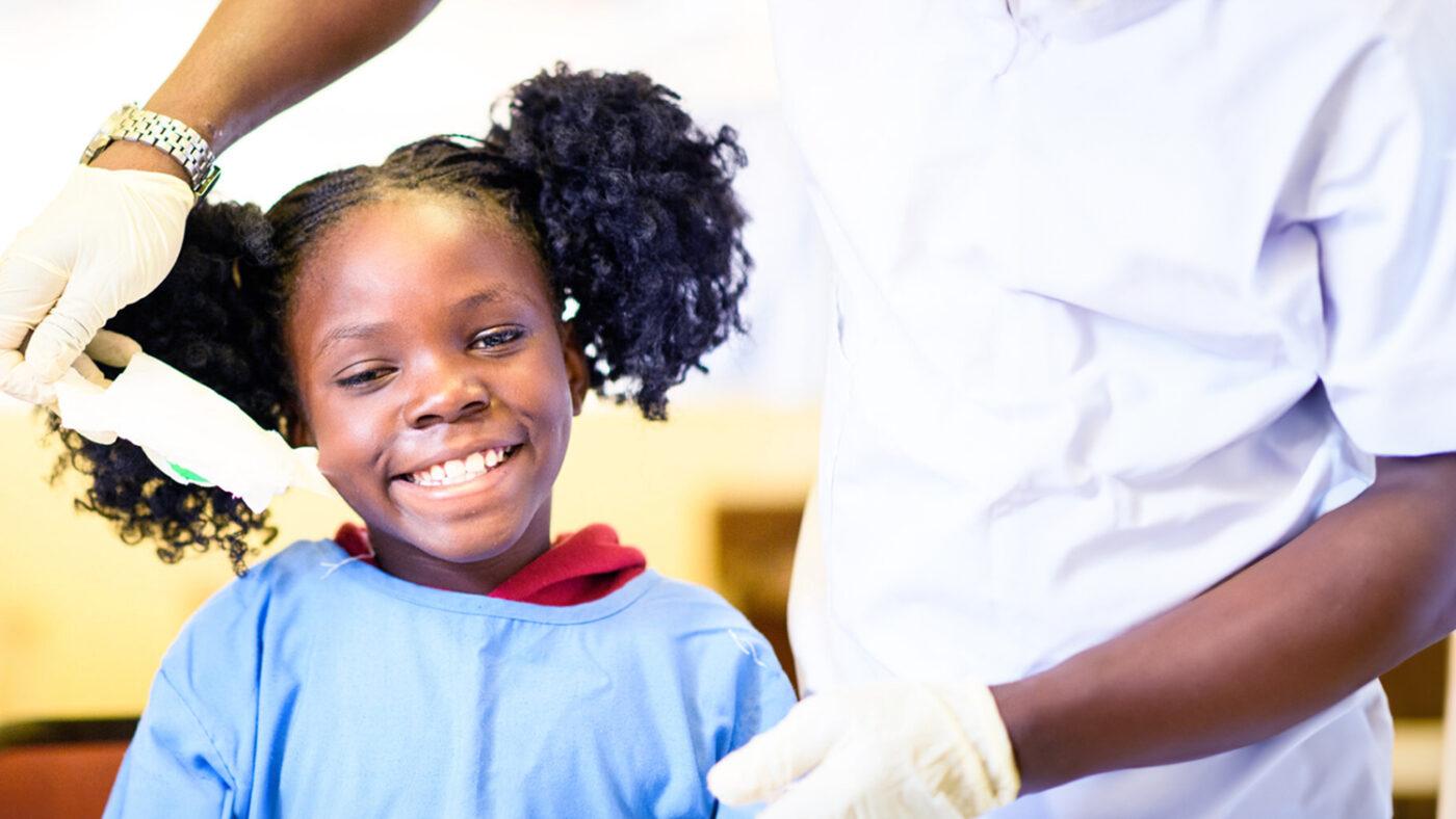 Luyando smiles as a health worker removes a bandage from her eyes. She's wearing a blue hospital gown.