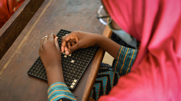 A young woman uses a board to learn braille.