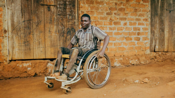 A young man using a wheelchair sits near a building.