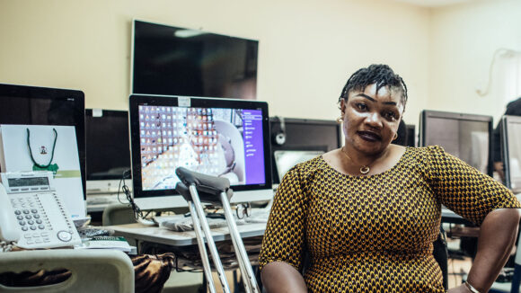 A woman sits next to a computer with crutches next to her.